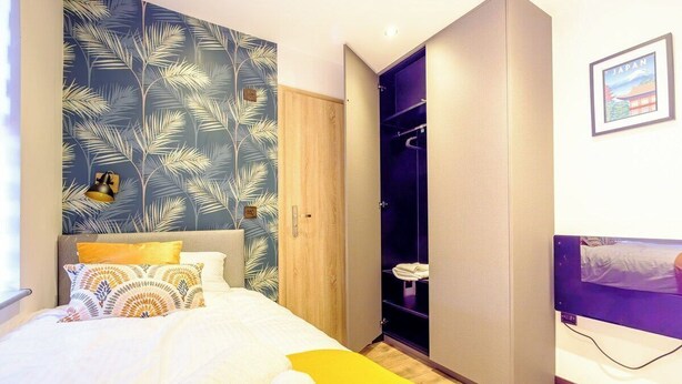 Ein Schlafzimmer mit einem Bett, einem Kleiderschrank und einer Wand mit Blättermuster.
