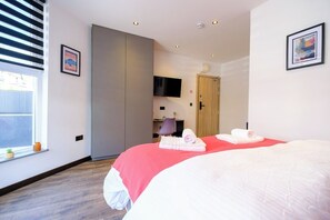 Ein Hotelzimmer mit Bett, Fernseher, Schreibtisch und Tür.