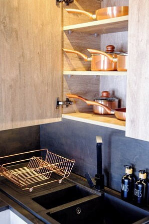 A kitchen with wooden cabinets, copper cookware, a black sink, and a metal drying rack. - Curzon a family & Pet friendly house with Hot Tub (Conwy Principal Area)