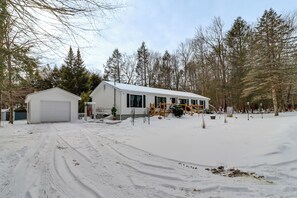 Una casa de dos pisos amb un garatge, envoltada de terra i arbres coberts de neu.