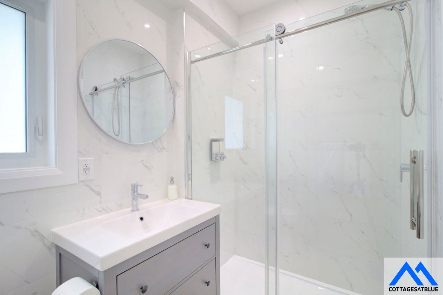 A modern bathroom with a glass-enclosed shower, a round mirror, and a white vanity with a sink.