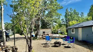 Ein Garten mit Baum, Grill, blauen Stühlen und einem Gartenhaus.