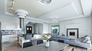 A modern kitchen with a central island, a dining area with a long table, and a living area with a large L-shaped sofa.