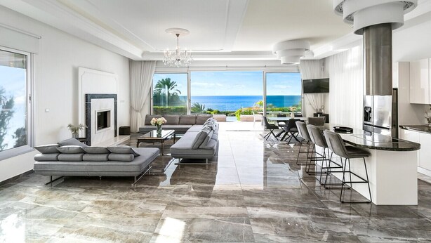 A modern living room with a large sofa, a TV, and a view of the ocean.