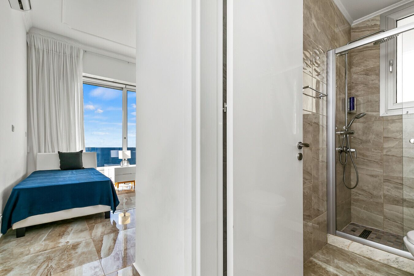 A bedroom with a bed, a window with curtains, and a view of the sea.
