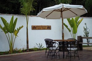 An outdoor patio with a wooden table and chairs, a white umbrella, and a sign that reads "Pousada da Isa". - Pousada da Isa (Quatro Barras)