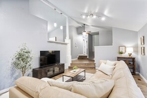 Una sala de estar moderna con un sofá color beige, una mesa de centro de madera y un televisor sobre un mueble oscuro.