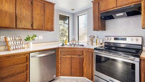 A kitchen with wooden cabinets, a stainless steel dishwasher, an oven, and a window providing natural light. - Two Living Spaces • Private Downstairs Suite (Grants Pass)