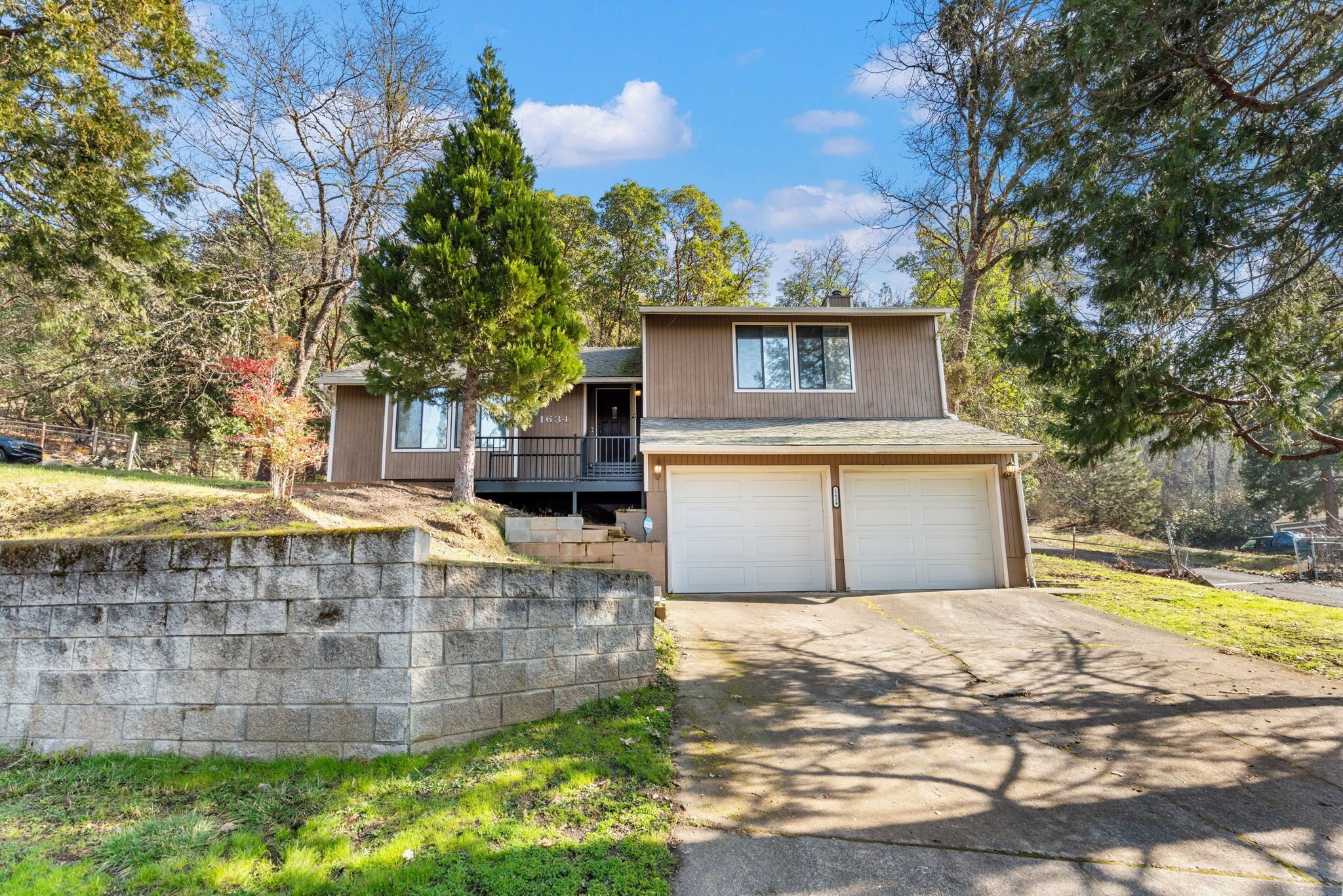 A two-story house with a garage, a stone retaining wall, and a driveway leading to the garage.