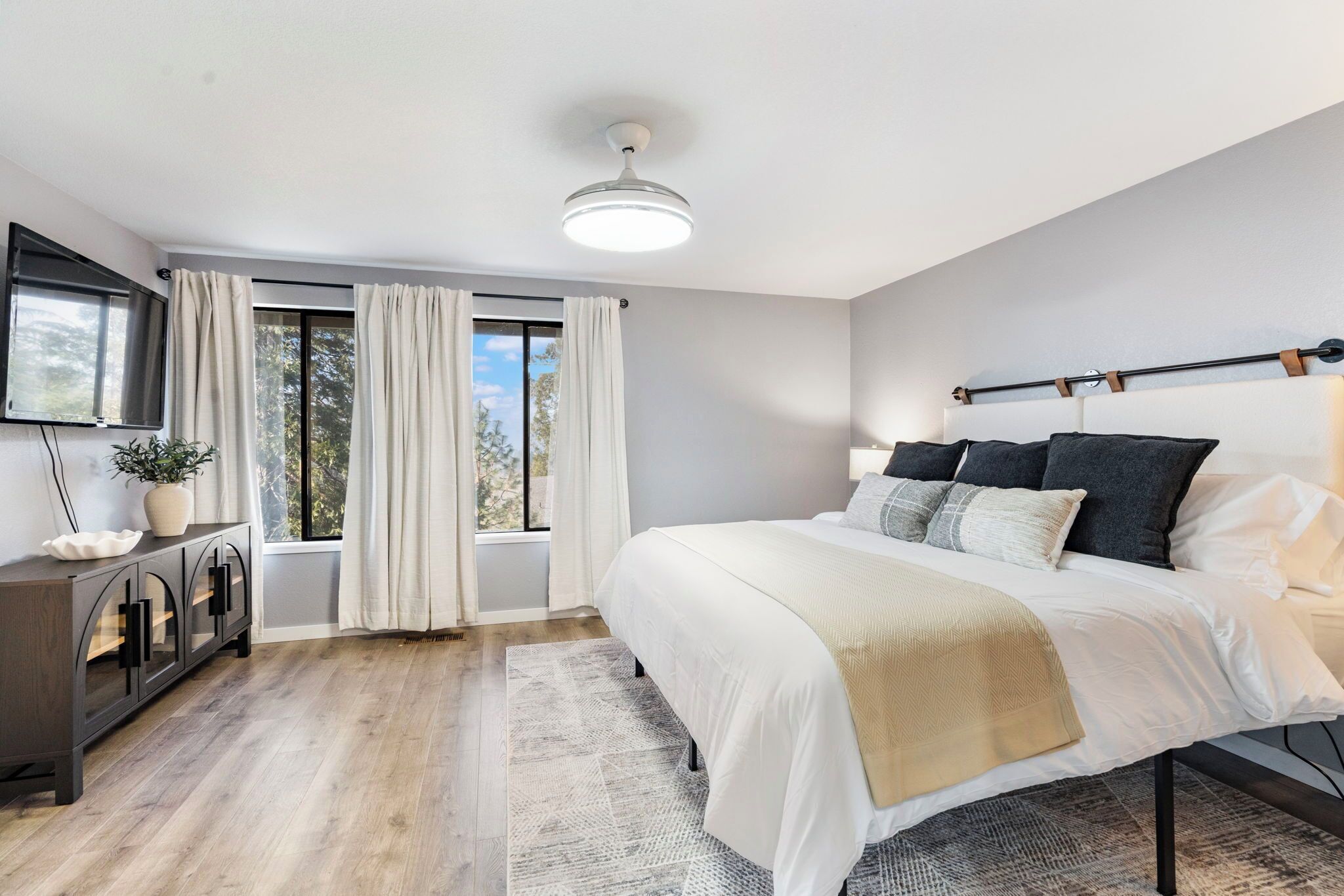 A bedroom with a large bed, a bedside table, a TV mounted on the wall, and a window with curtains.