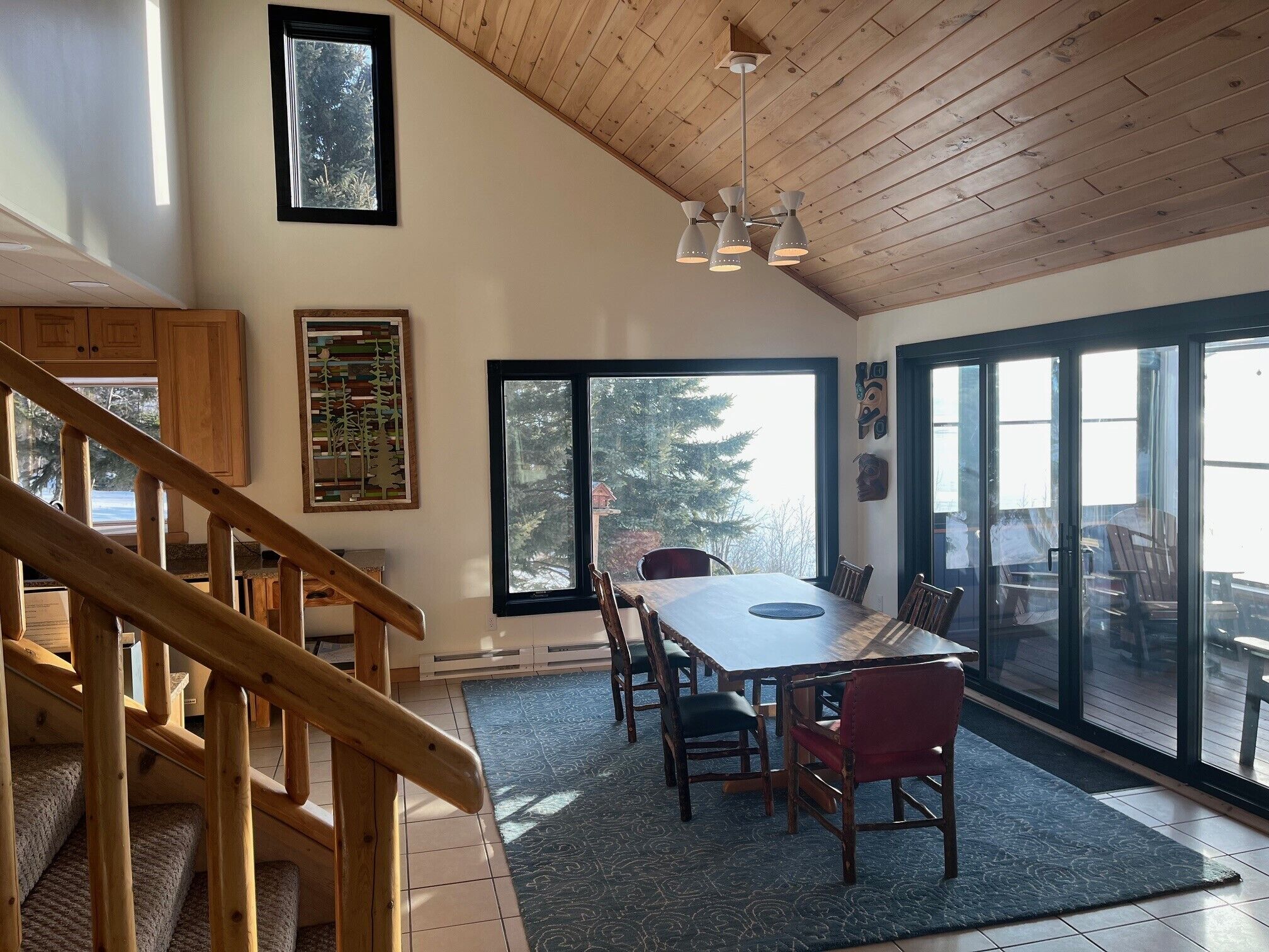 A dining area with a large table, chairs, and a view of the outdoors through large windows.