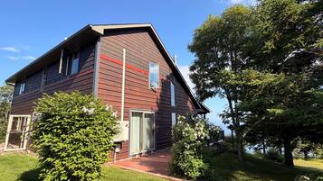 A two-story wooden house with a red roof, a front door, and a small porch.