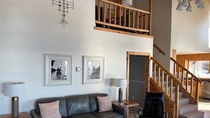 A living room with a leather sofa, two framed pictures, a wooden coffee table, a lamp, and a staircase leading to a second floor. - Halsnoy Haven New Listing. Iconic property! (Tofte)