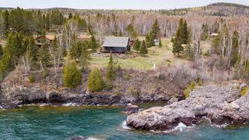A cabin surrounded by forest, a rocky shoreline, and a river.