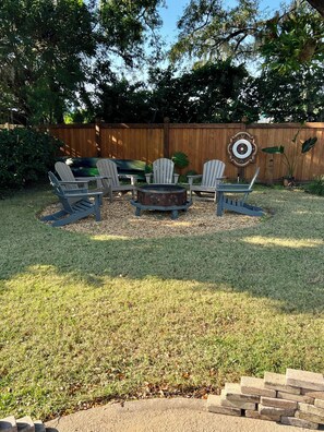 A backyard with a wooden fence, a fire pit, and three Adirondack chairs. - 150-Yards To Arnold Palmer’s Bay Hill Clubhouse! (Orlando)