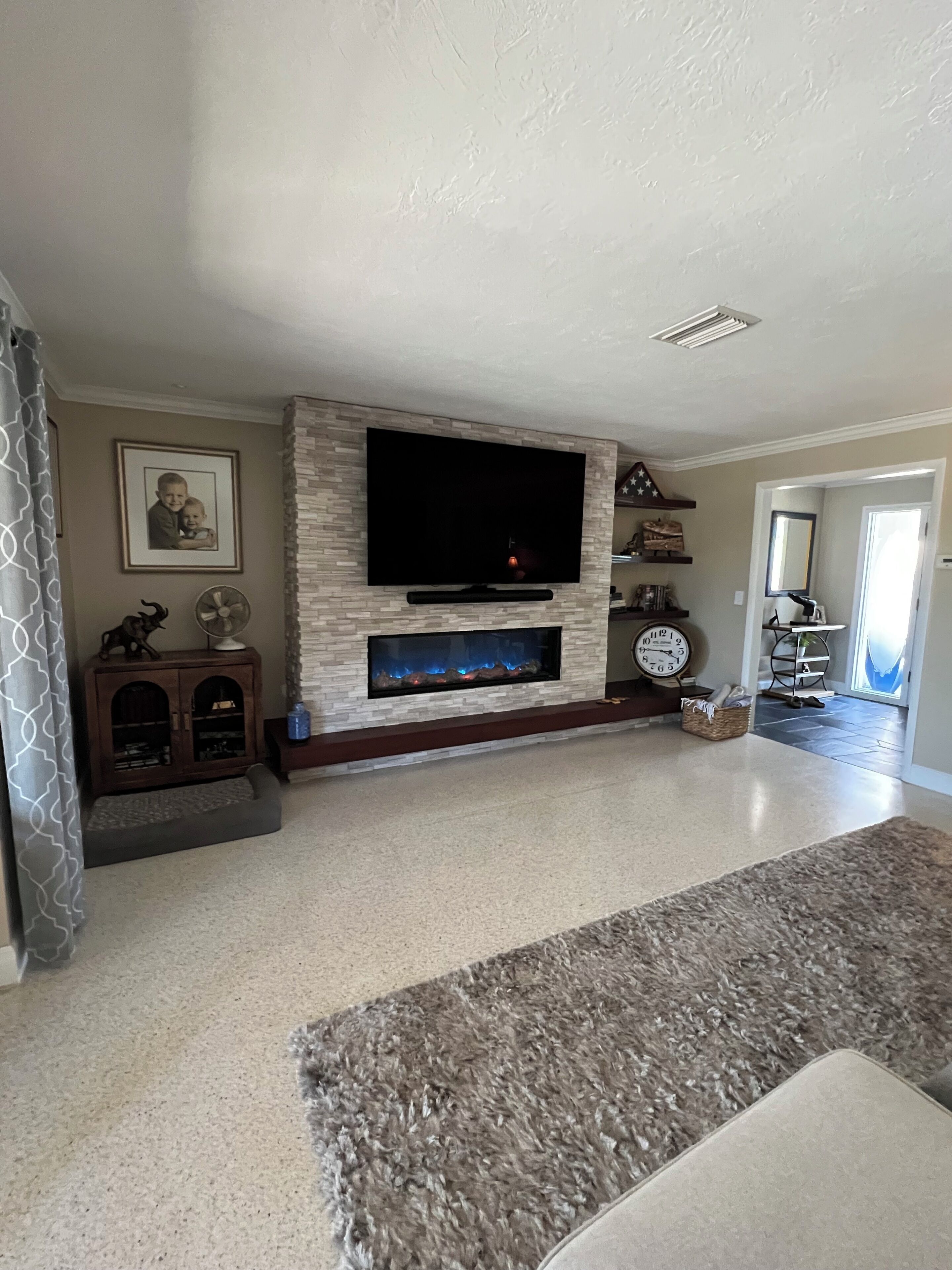 A living room with a stone fireplace, a flat-screen TV, a wooden cabinet, and a large rug.