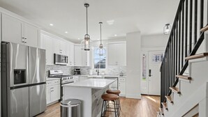 A modern kitchen with stainless steel appliances, white cabinetry, and a central island with stools. - Modern & Stylish 2/2.5 Home Mainstreet Clayton! (Clayton)