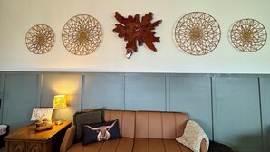Un salón con un sofá de cuero marrón, un tapete estampado y decoración de pared con diseños circulares y con forma de hojas.