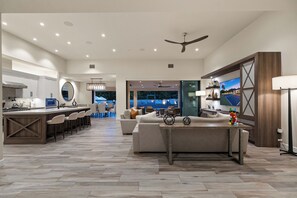A spacious living area with a kitchen, dining area, and a view of an outdoor pool. - Pura Vida - Luxe Estate w/ Pool, Spa & Pickleball! (Rancho Mirage)