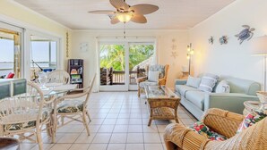 A spacious living area with a ceiling fan, wicker furniture, a glass coffee table, and a view through the sliding glass door.