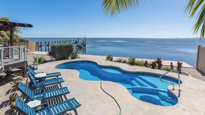 A swimming pool with a view of the ocean, surrounded by lounge chairs and a wooden deck.
