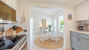 Cocina moderna con comedor, que incluye una isla central, sillas blancas y una cafetera.