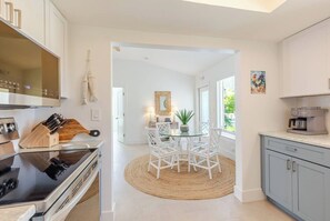 A modern kitchen with a dining area, featuring a central island, white chairs, and a coffee machine. - Beach House 5BR/5BA, 1/2 mile to Sombrero Beach, Pool & 75ft Dockage, Newly Renovated (Marathon)