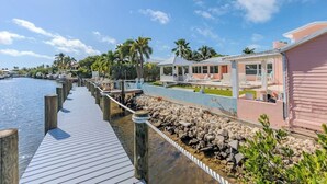 Una propiedad frente al agua con muelle de madera, zona de piscina y un edificio de fachada rosa.