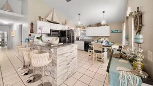 Una cucina moderna con isola centrale, mobili bianchi, elettrodomestici in acciaio inossidabile e un'area pranzo con tavolo e sedie.