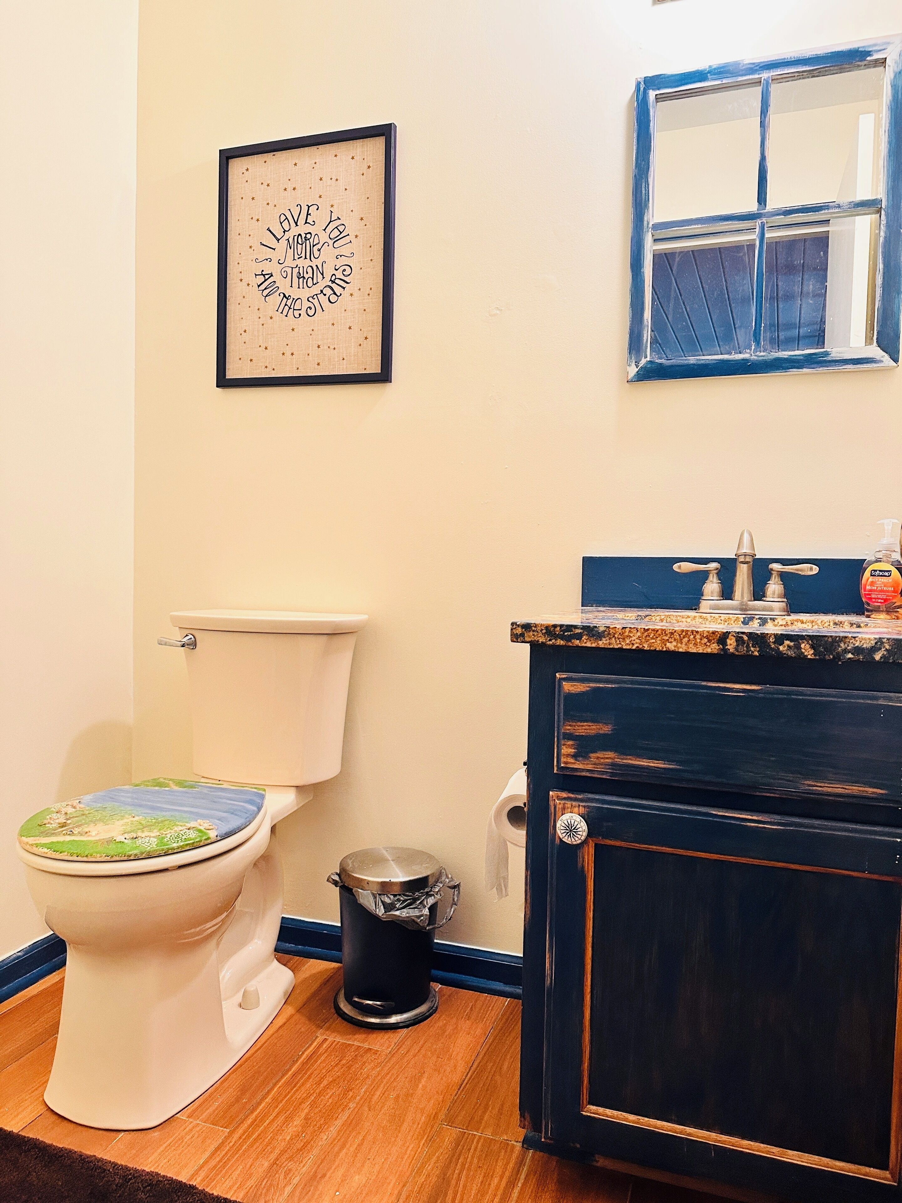 Casa de banho com sanita, lavatório com espelho e uma frase emoldurada na parede.