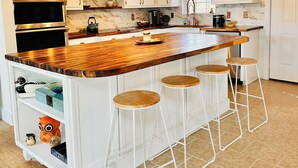 Cocina con techo de madera, armarios blancos, una isla grande con taburetes y electrodomésticos de acero inoxidable.