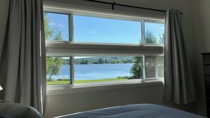 Une chambre avec un grand lit, une fenêtre avec des rideaux et une vue sur un lac.