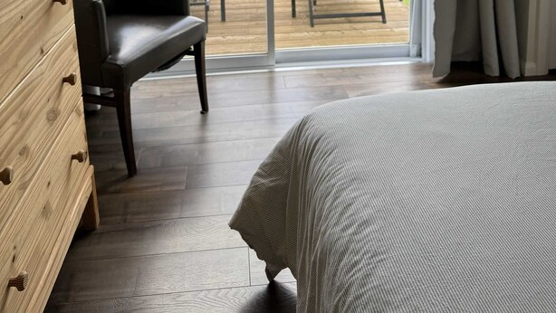 Une chambre avec une grande fenêtre, un lit, une commode en bois et deux chaises placées face à une vue sur un lac et la verdure.