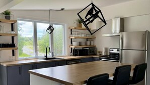 Une cuisine moderne dotée d’un grand îlot central, de tabourets de bar, d’un four encastré et offrant une vue sur la verdure environnante.