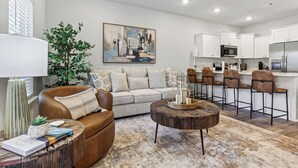 A modern living room with a sofa, coffee table, and bar stools. - Brand-new Coastal Escape 3BR/2.5BA minutes from vibrant downtown Ocean Springs. (Ocean Springs)