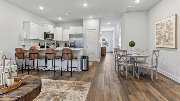 A modern kitchen with white cabinets, a stainless steel refrigerator, and a dining area with a round table and chairs. - Brand-new Coastal Escape 3BR/2.5BA minutes from vibrant downtown Ocean Springs. (Ocean Springs)