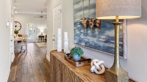 A hallway with a wooden reception desk, a large painting of sailboats, a lamp, and a potted plant. - Brand-new Coastal Escape 3BR/2.5BA minutes from vibrant downtown Ocean Springs. (Ocean Springs)