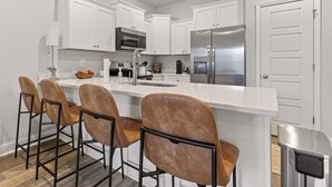 A modern kitchen with white cabinets, stainless steel appliances, and a central island with bar stools. - Brand-new Coastal Escape 3BR/2.5BA minutes from vibrant downtown Ocean Springs. (Ocean Springs)