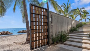 Un mur de béton avec un portail en métal, des palmiers et une plage en arrière-plan.