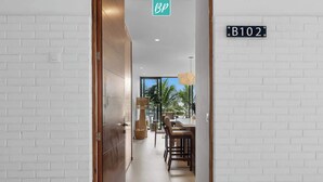 Un couloir avec un mur en briques blanches, une porte en bois et une pancarte indiquant le numéro de la pièce : B102.