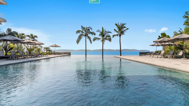 Un espace piscine avec des chaises longues et des parasols, des palmiers et une vue sur la mer.