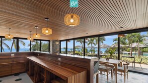 Un espace bar moderne, doté de mobilier en bois, de grandes fenêtres et de luminaires suspendus en osier.