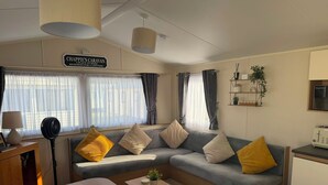 Un espacio de sala acogedor con un sofá, una mesita de centro y una mesa de comedor. Hay un letrero sobre el sofá que dice 'CHAPPIE'S CARAVAN'.