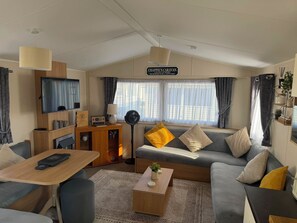 A modern living room with a sofa, coffee table, TV, and a sign above the sofa. - Chappie's Caravan 1.0 (Rhyl)