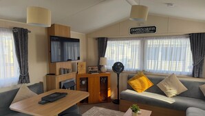 A cozy living room with a sofa, a coffee table, a TV, and a sign that reads 'Chappie's Caravan.'