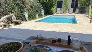A poolside dining setup with a tray containing a salad and two plates of bread, a glass of water, and sunglasses on a wooden table. - Family villa in the heart of the Vaucluse (Sorgues)