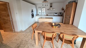 A modern kitchen with white cabinets, a wooden dining table, and wicker chairs. - Family villa in the heart of the Vaucluse (Sorgues)