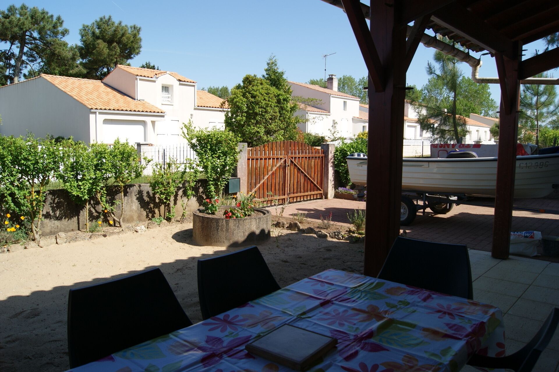 A covered outdoor seating area with a table set for dining, surrounded by a garden with plants and a wooden fence.