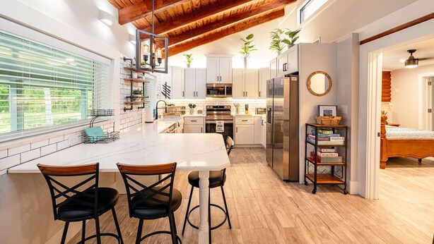 A modern kitchen with white cabinets, a central island with bar stools, and a wooden ceiling. - The Cabin – 3BR Log Retreat w/Outdoor Bar & Grill (Jupiter)