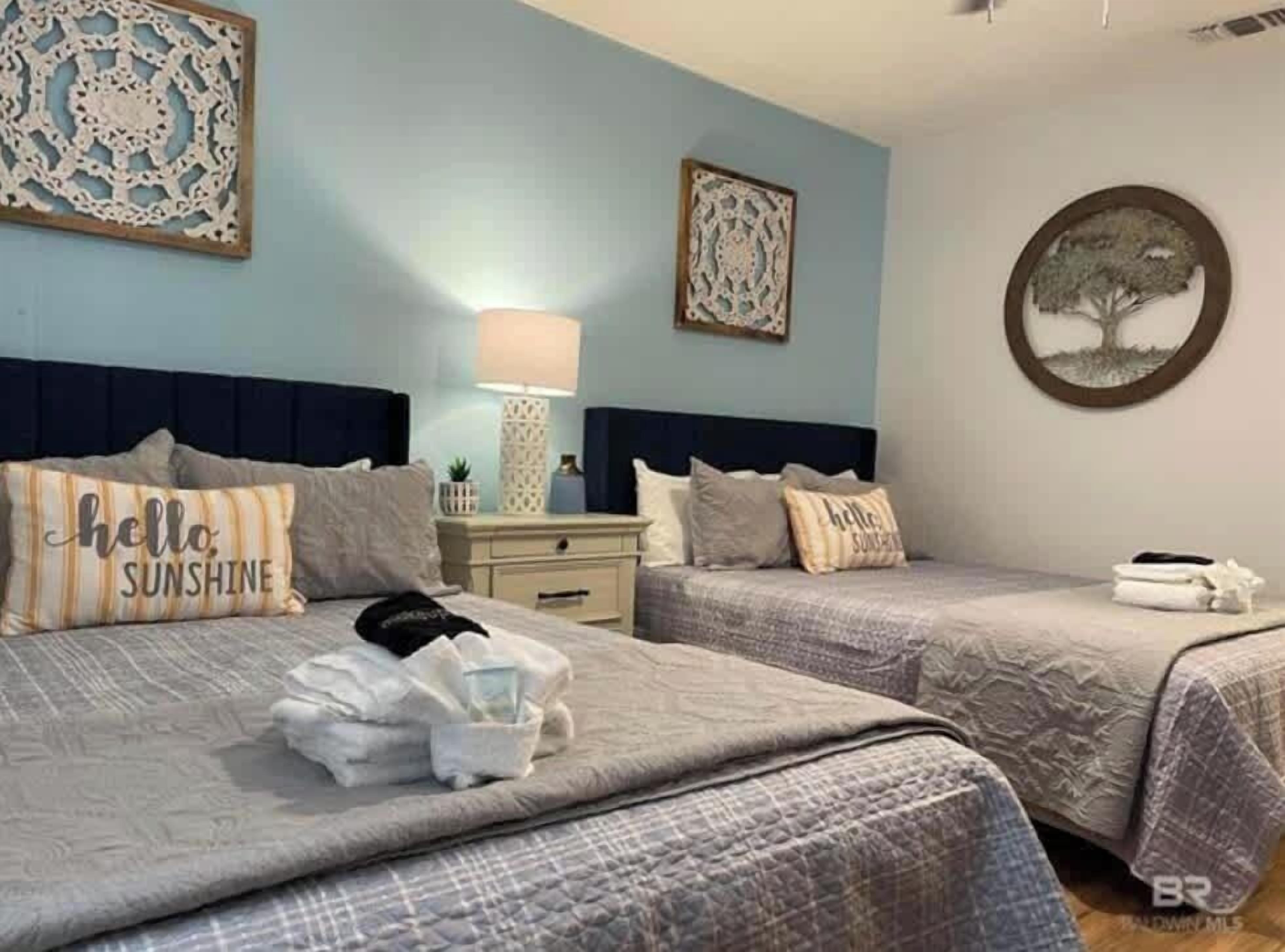 A bedroom with two beds, a nightstand, a lamp, and decorative wall art.